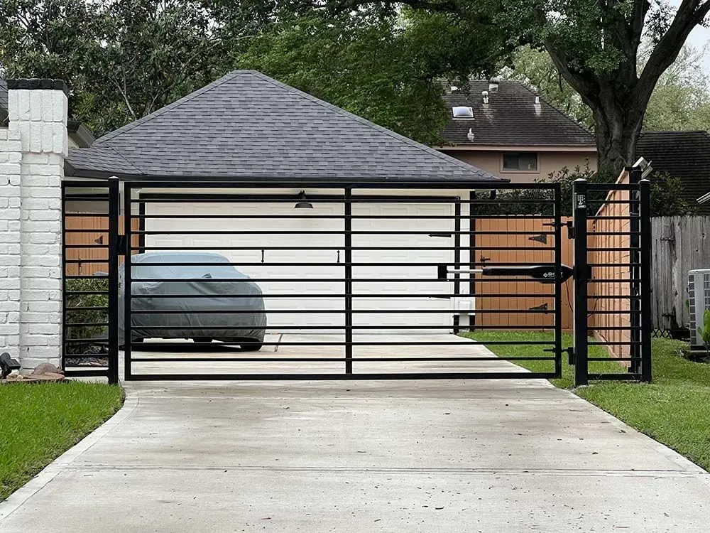 Black metal driveway gate with horizontal bars in front of a garage, on a concrete driveway.