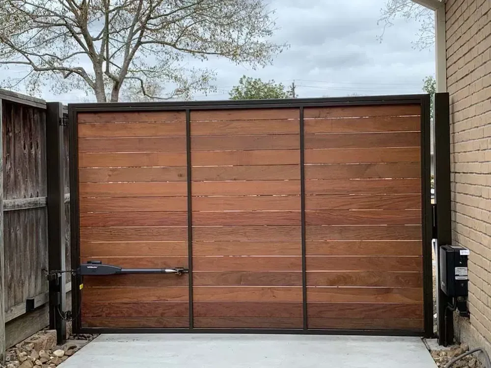 Wooden gate with a black metal frame, automated opener, and concrete pad.