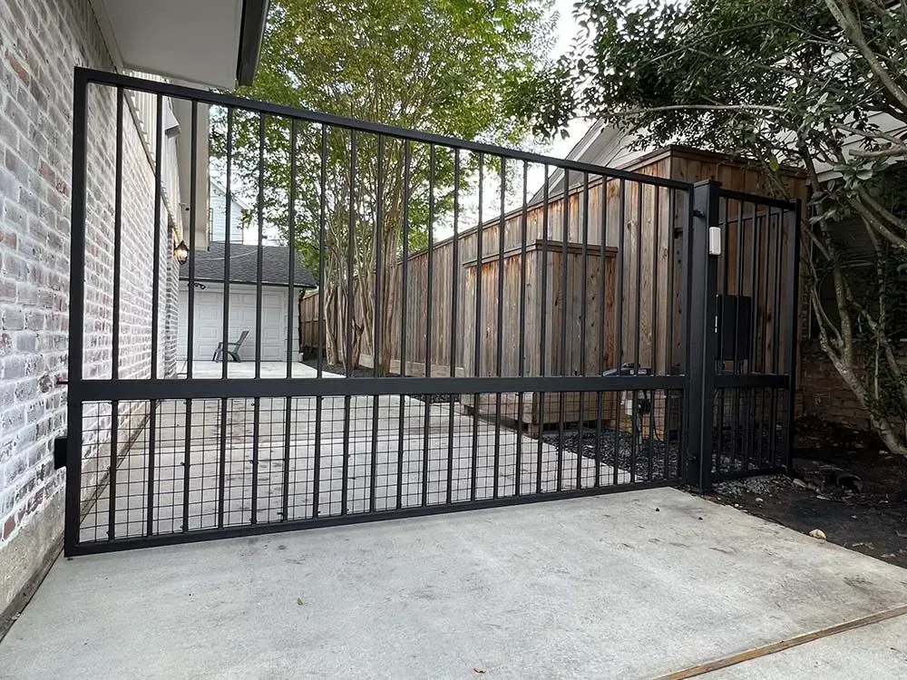 Black metal gate on a concrete patio, next to a brick wall and wooden structure.