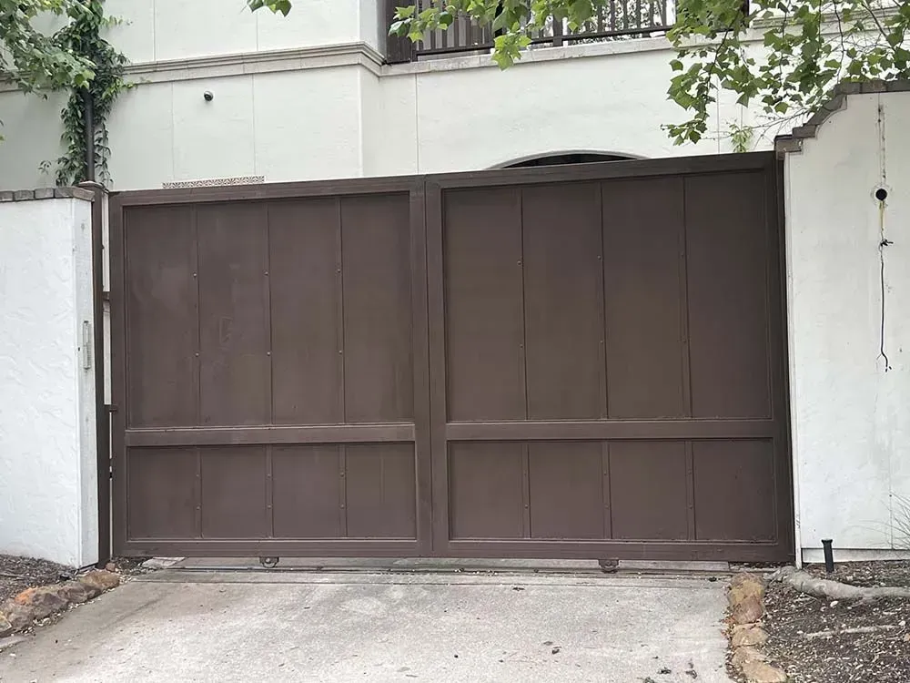 Brown gate with vertical planks, in front of a white wall.