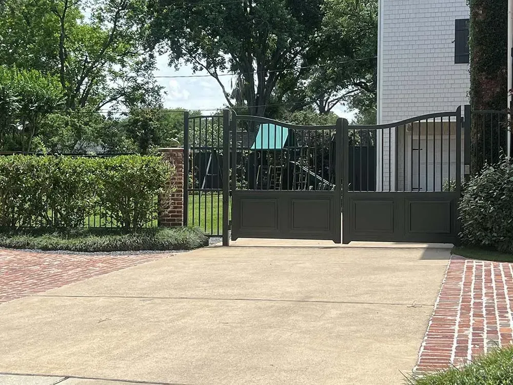 Gray metal driveway gate open, facing a concrete driveway. Brick house in background.