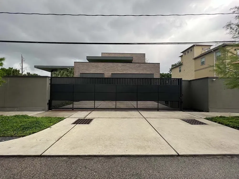 Modern home behind a black gate on a concrete driveway, under a cloudy sky.