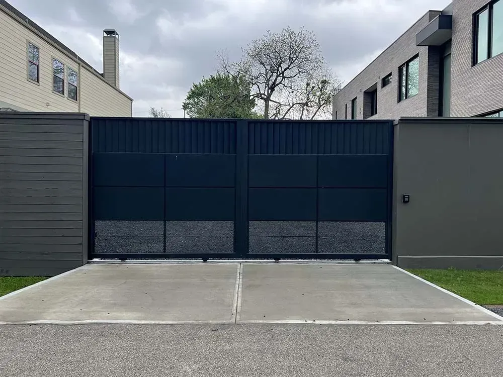 Dark blue metal gate, concrete driveway, flanked by modern buildings, overcast sky.