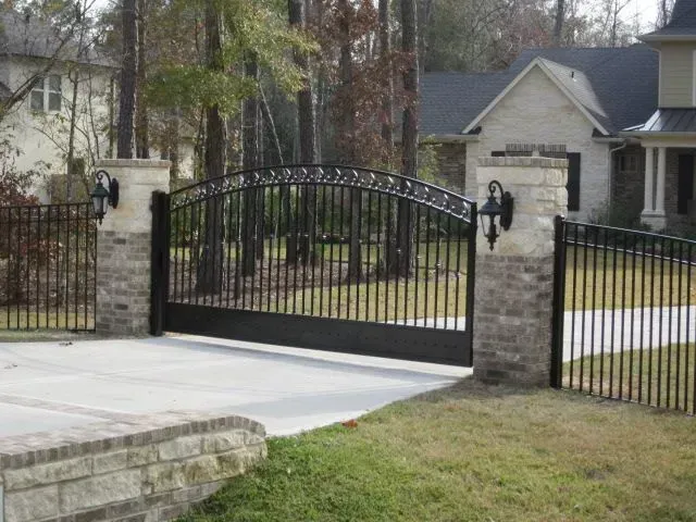 Black wrought iron driveway gate with brick and stone pillars; residential setting.