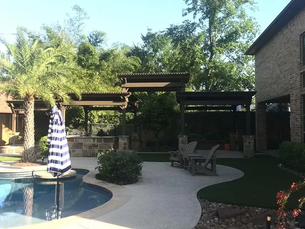 Backyard with pool, patio, and brown pergola with seating, next to a brick house.