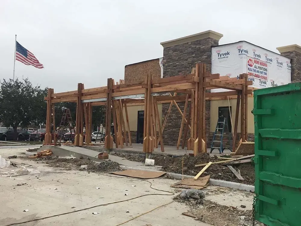 Restaurant under construction, exterior view. Wooden beams frame the front, building covered in Tyvek. American flag.