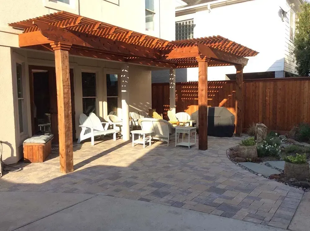 Wooden pergola over a patio with seating; pavers on ground.