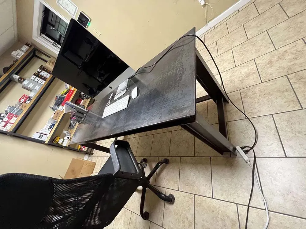 Black desk with dual monitors, chair, and computer accessories in an office setting.
