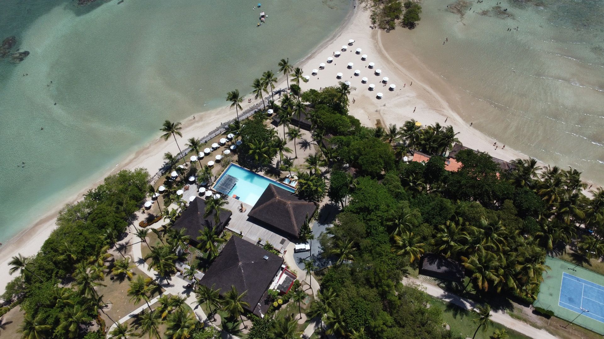 Vista aérea de um resort com piscina, edifícios, palmeiras e praias.