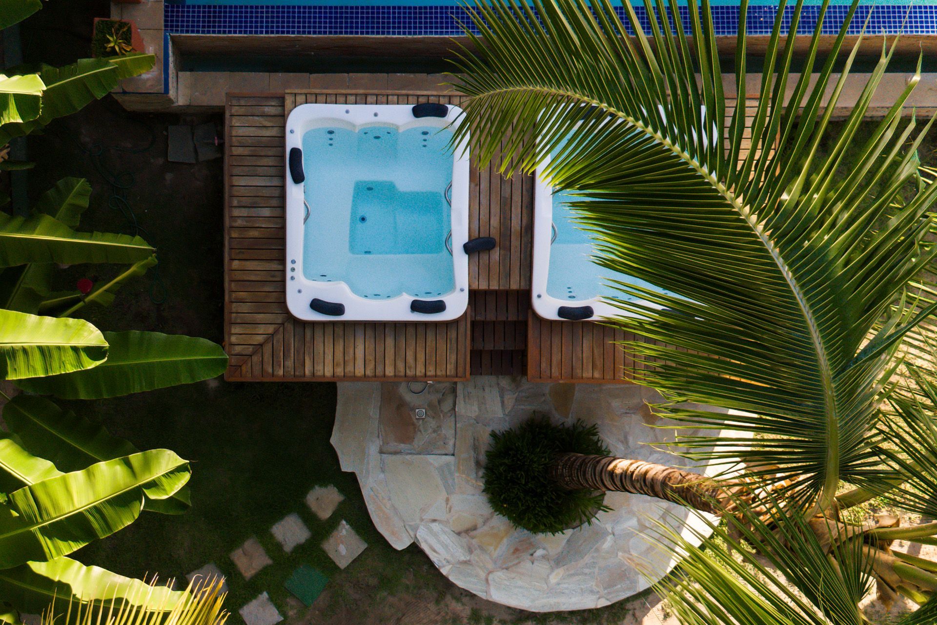 Mulher recebendo uma massagem na testa ao ar livre; mãos, folhagens verdes e lençóis brancos são visíveis.