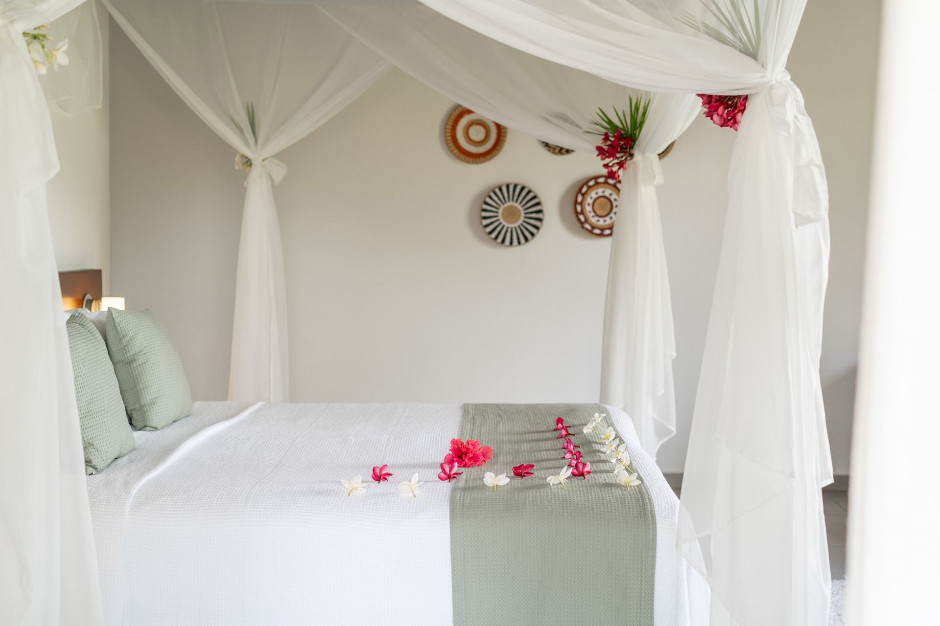 Quarto com cama de dossel, roupa de cama branca, almofadas verdes e decoração floral na cama e na parede.