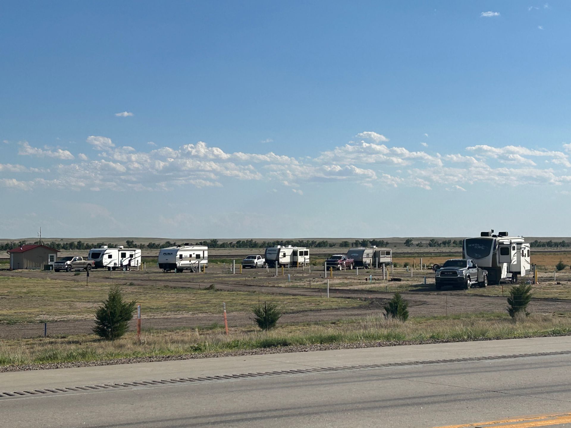 A row of rvs are parked in a field next to a road.