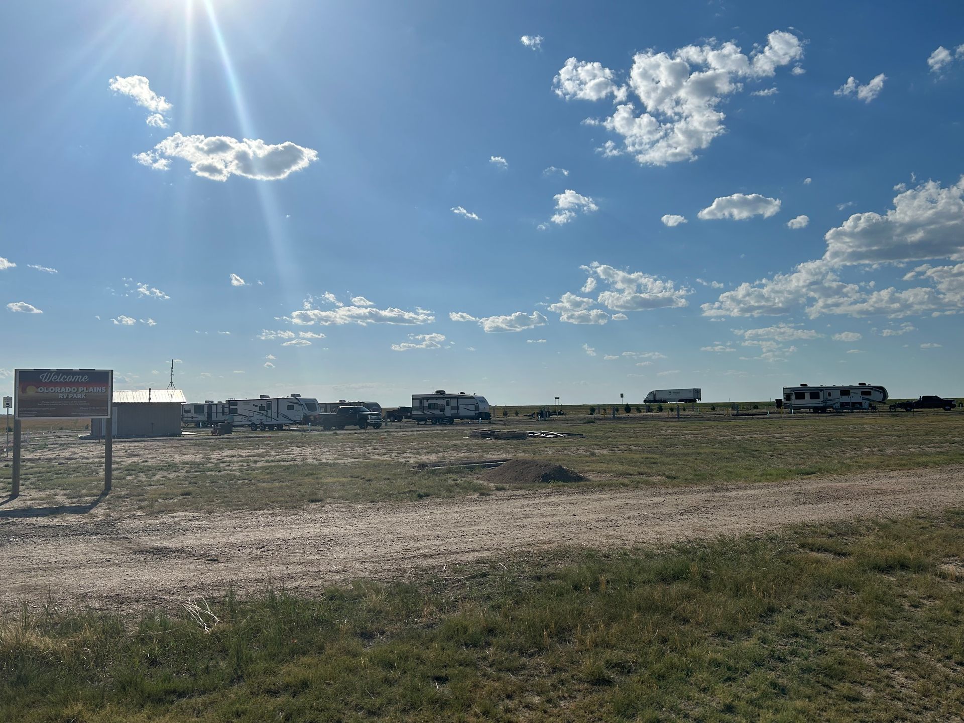 A dirt road going through a grassy field with a sign in the foreground.