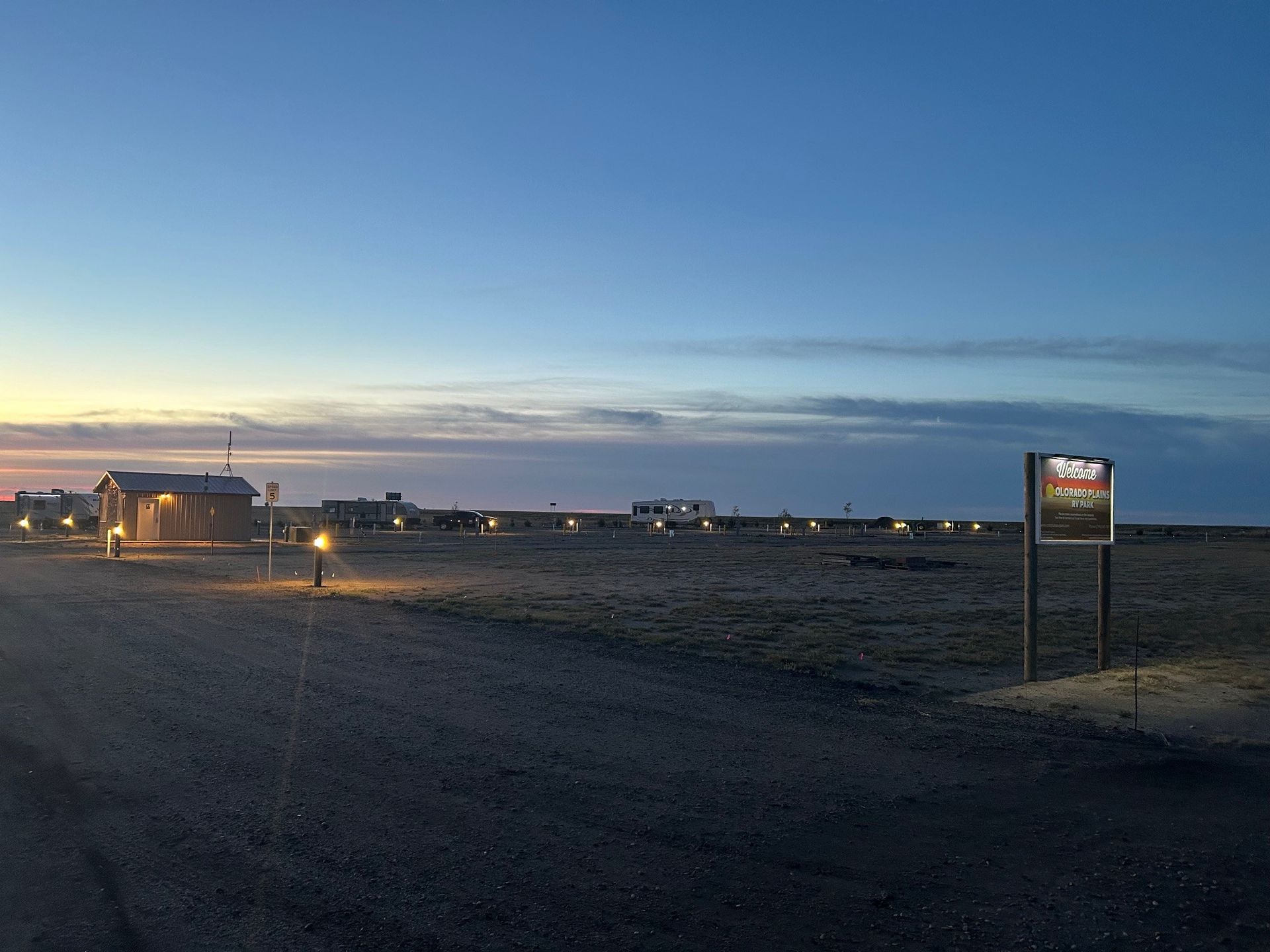 A dirt road with a sign in the middle of it and a sunset in the background.