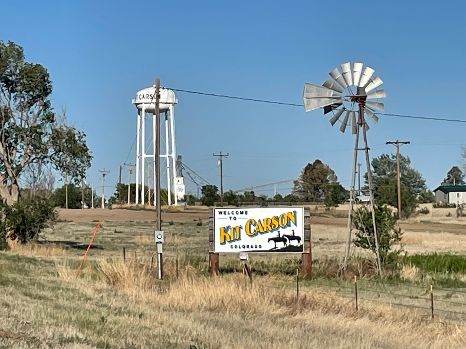A windmill in a field with a sign that says welcome to kit carson