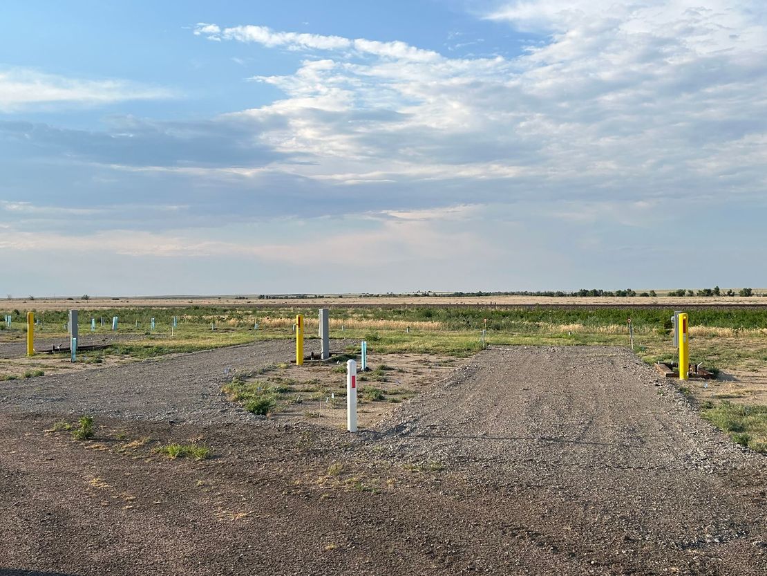 A gravel road going through a field with a blue sky in the background.