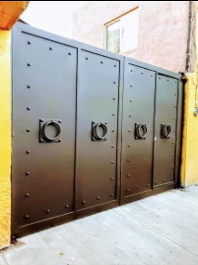 Una puerta de metal negra se encuentra al lado de una pared amarilla.