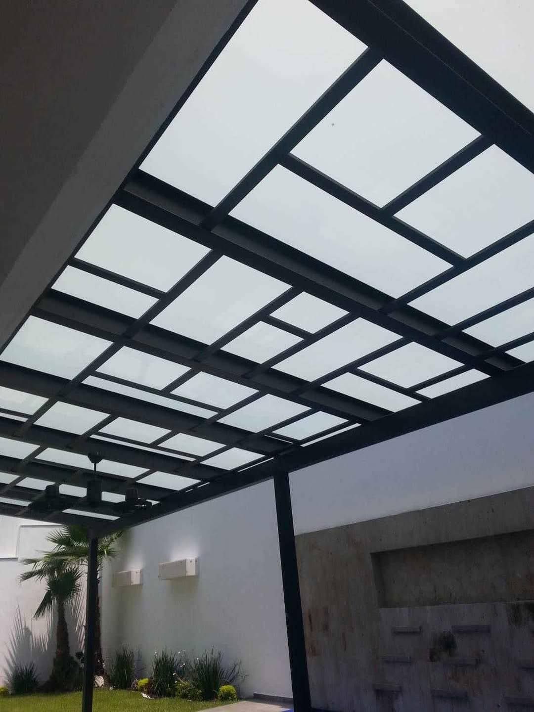 Una pérgola con techo de cristal transparente y marco negro.