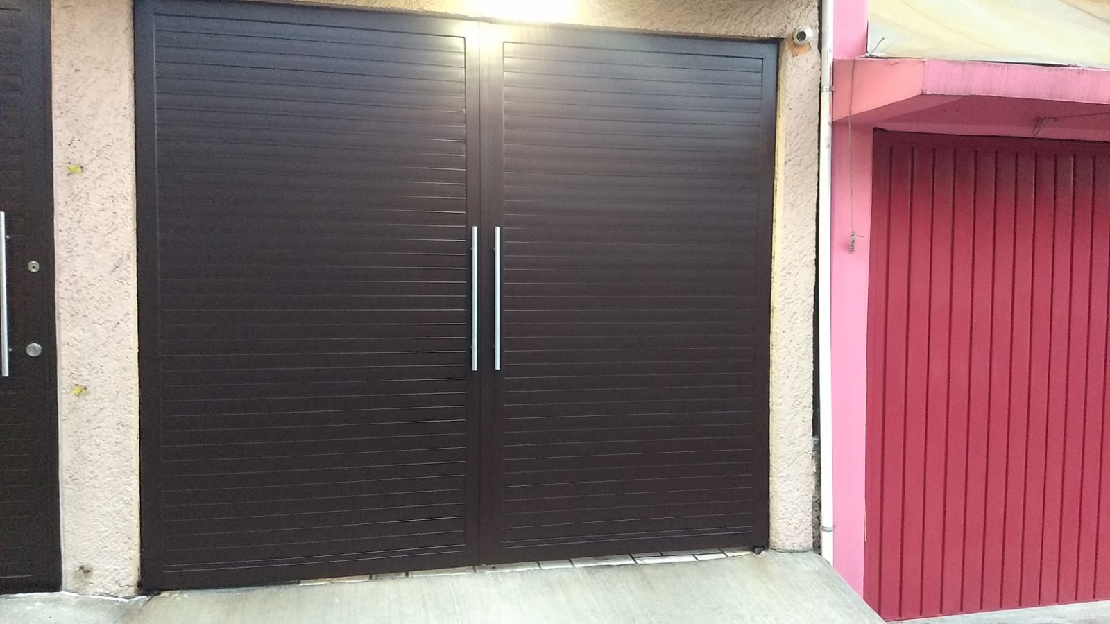 Una puerta de garaje negra está al lado de una puerta de garaje rosa.