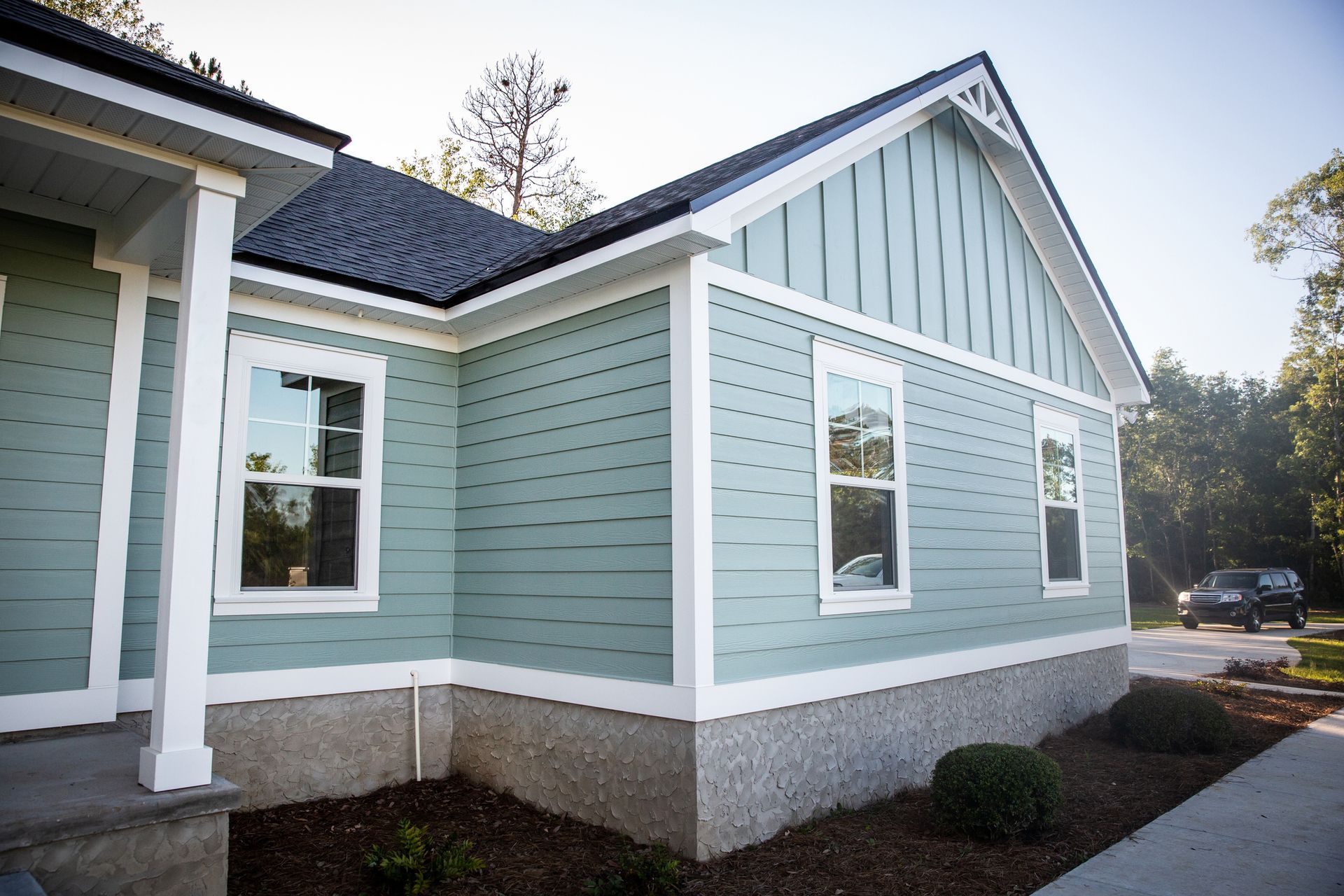 A light green house exterior with horizontal and vertical siding, white trim, and a grey foundation, set in a yard.