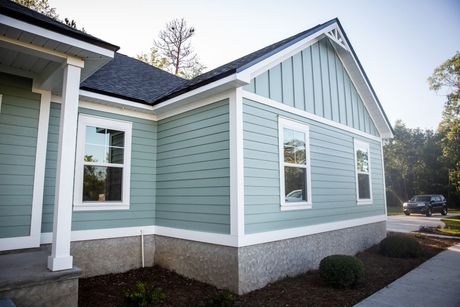 A house exterior with light blue horizontal and vertical siding, white trim, a dark roof, and a gray concrete foundation.