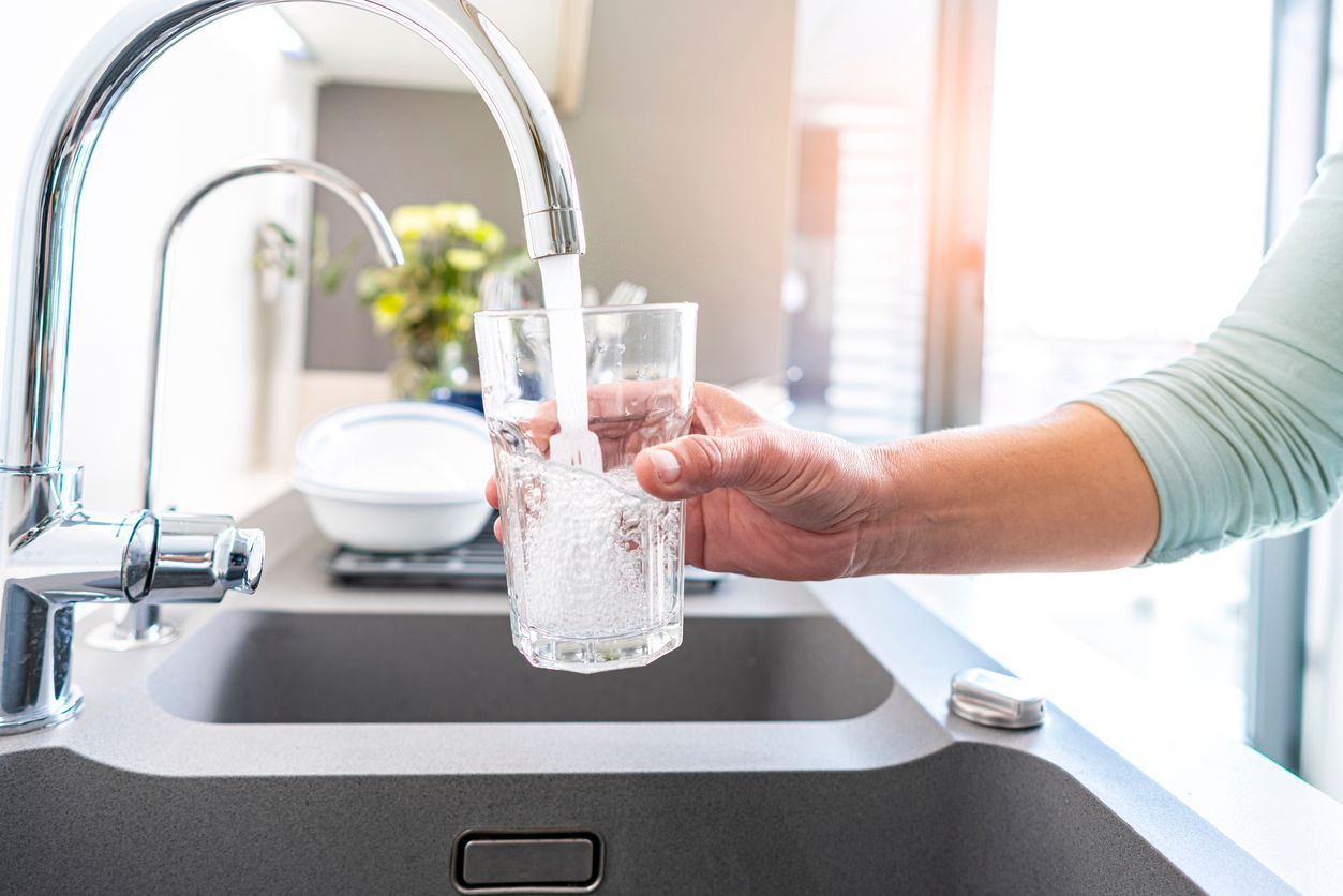 A person filling a clear glass with water from a kitchen faucet.