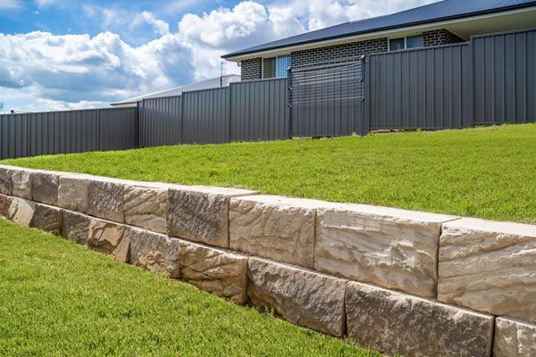 A stone wall surrounds a lush green lawn in front of a house.