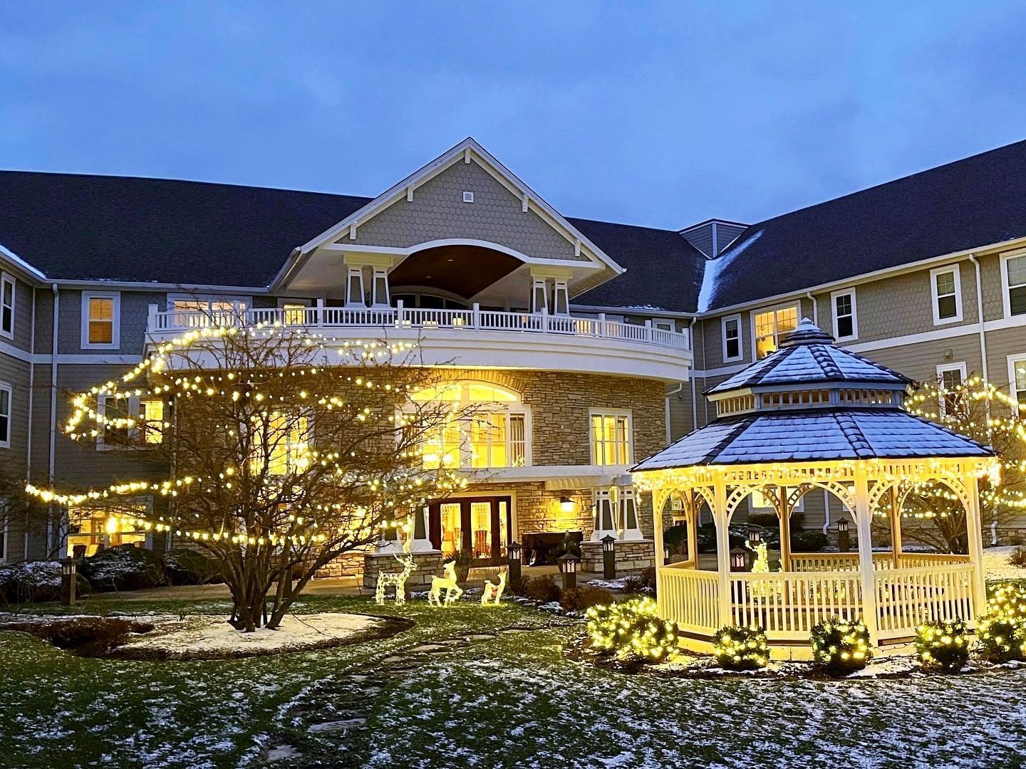 A snow-covered building at dusk decorated with Christmas lights; a gazebo is in the foreground.