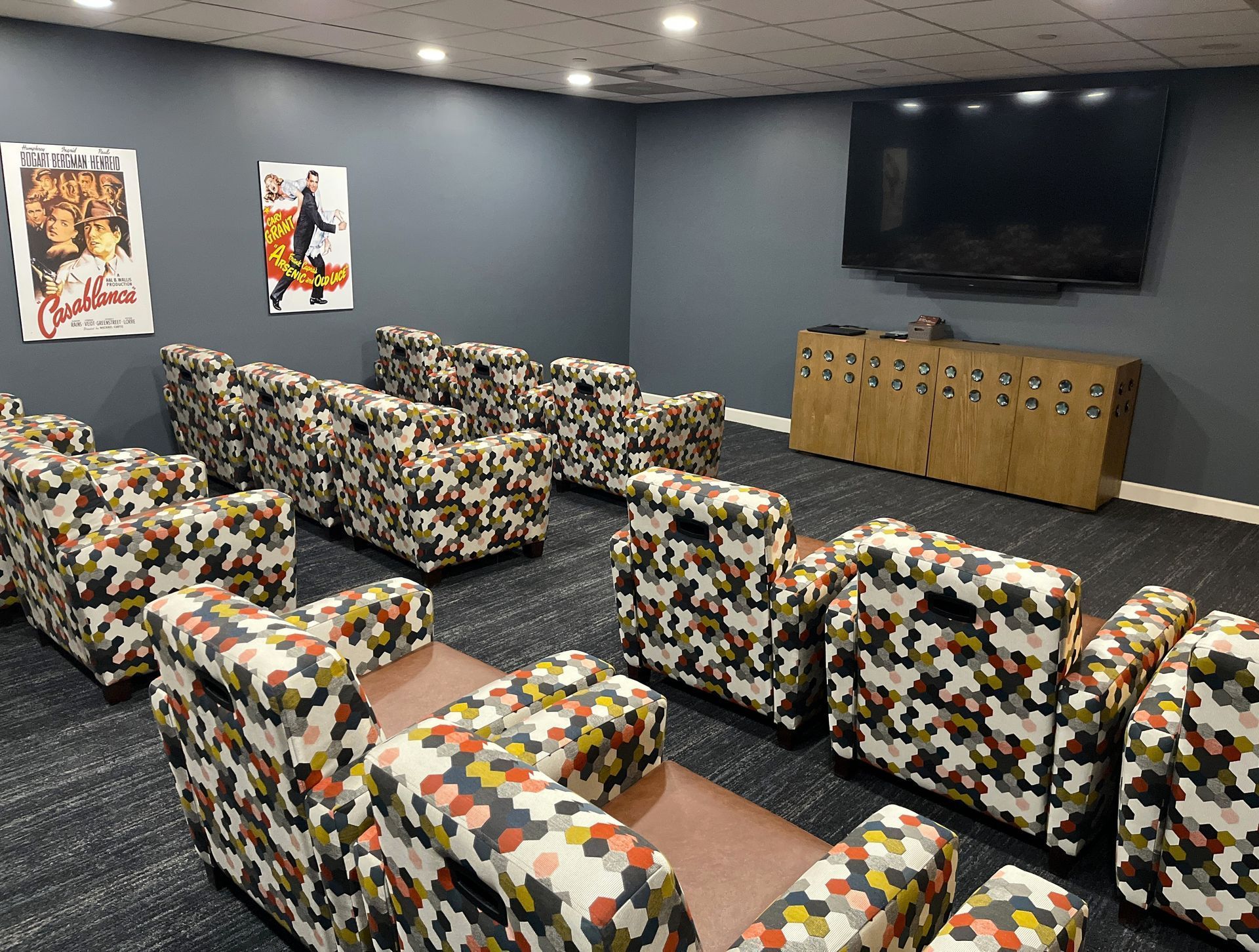 A small home theater with patterned armchairs. Movie posters are on the walls, and a TV is mounted on the wall.