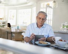 Retirement Living Communities — Senior Man Using Digital Tablet and Eating Breakfast in Glenview, IL
