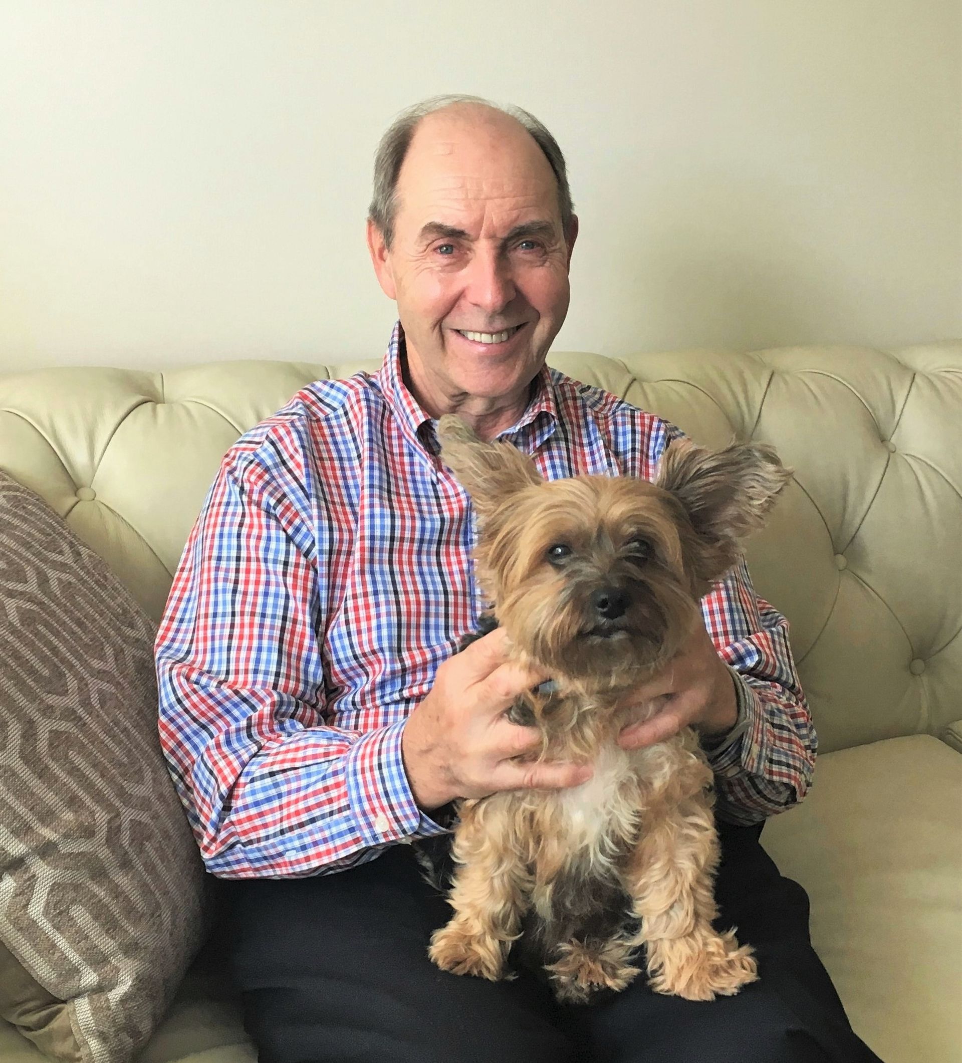 A man is sitting on a couch holding a small dog.