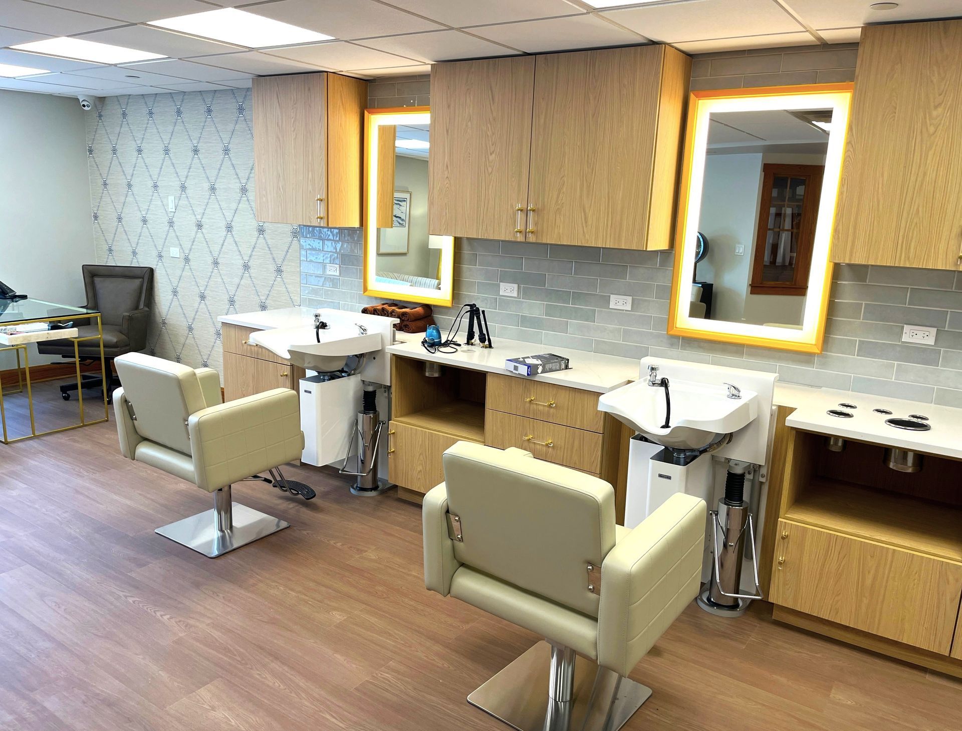 A salon with three hair-washing stations. Each station has a chair, sink, and mirror with blonde cabinetry and pale blue tile.