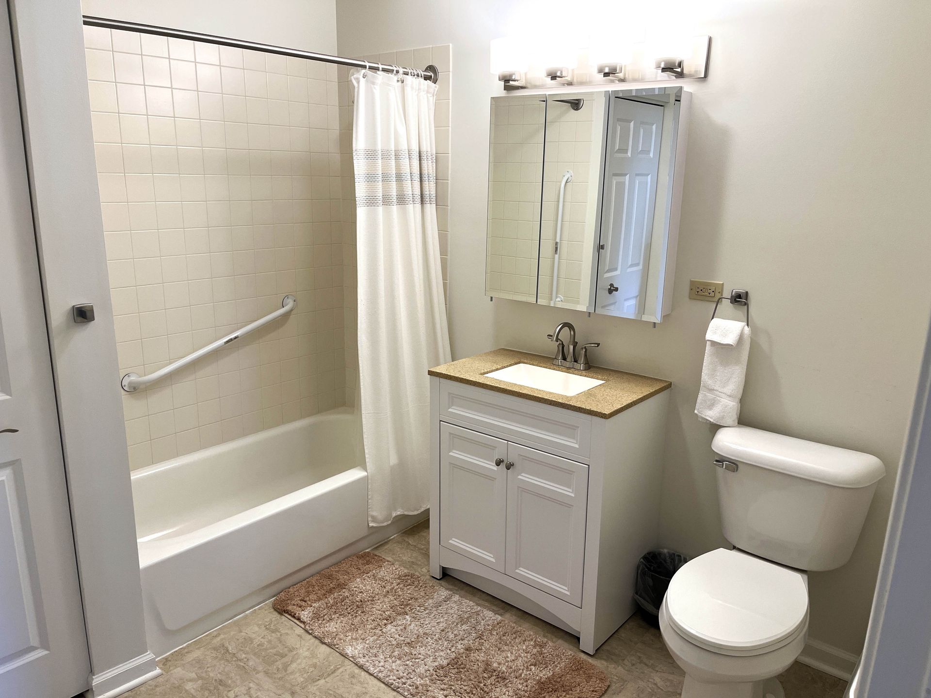 Bathroom with white tub, toilet, and vanity. Includes a shower curtain, mirror, and a grab bar.