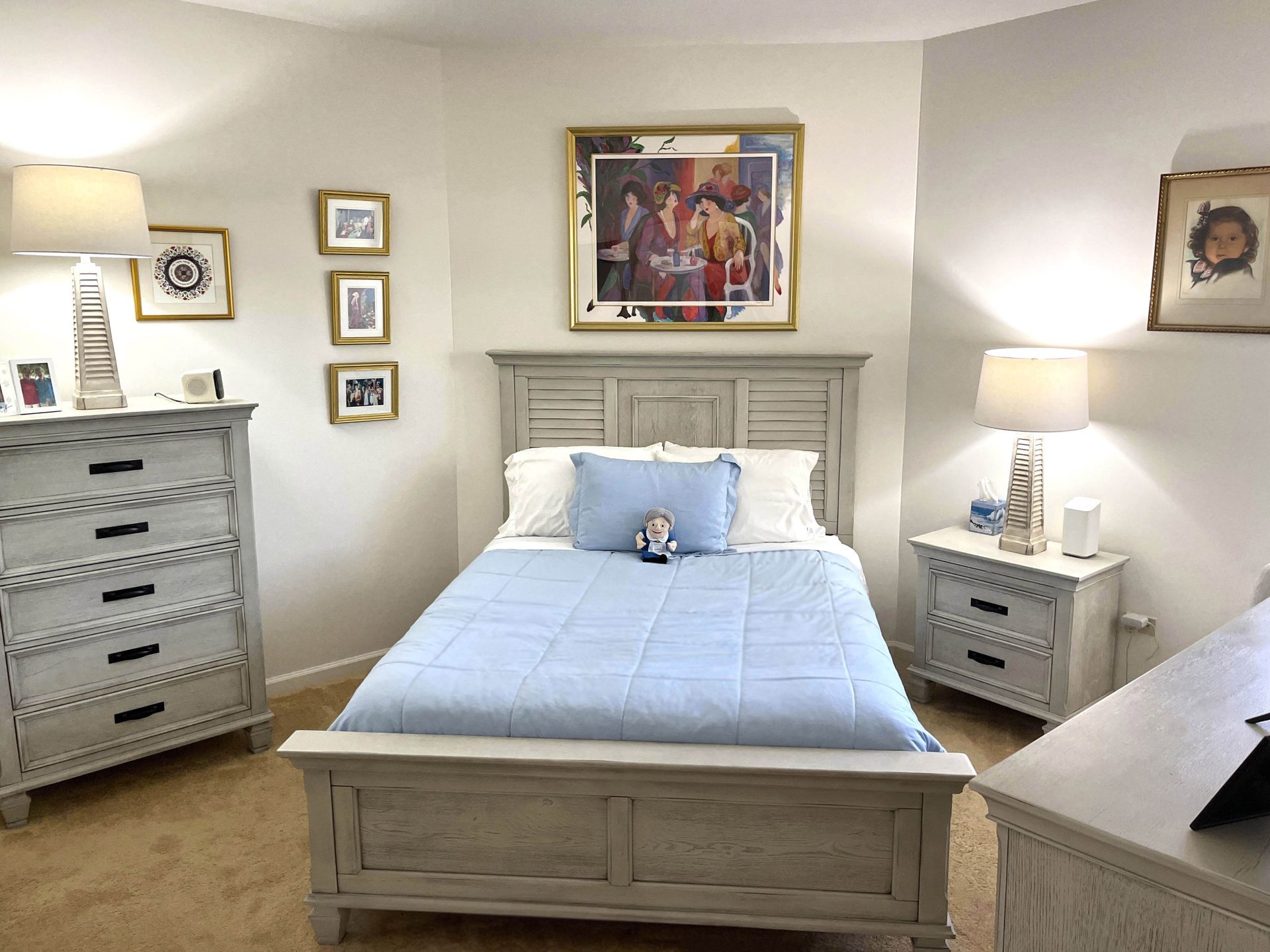 Bedroom with light blue bedspread, matching dresser and nightstand, and framed artwork on the wall.