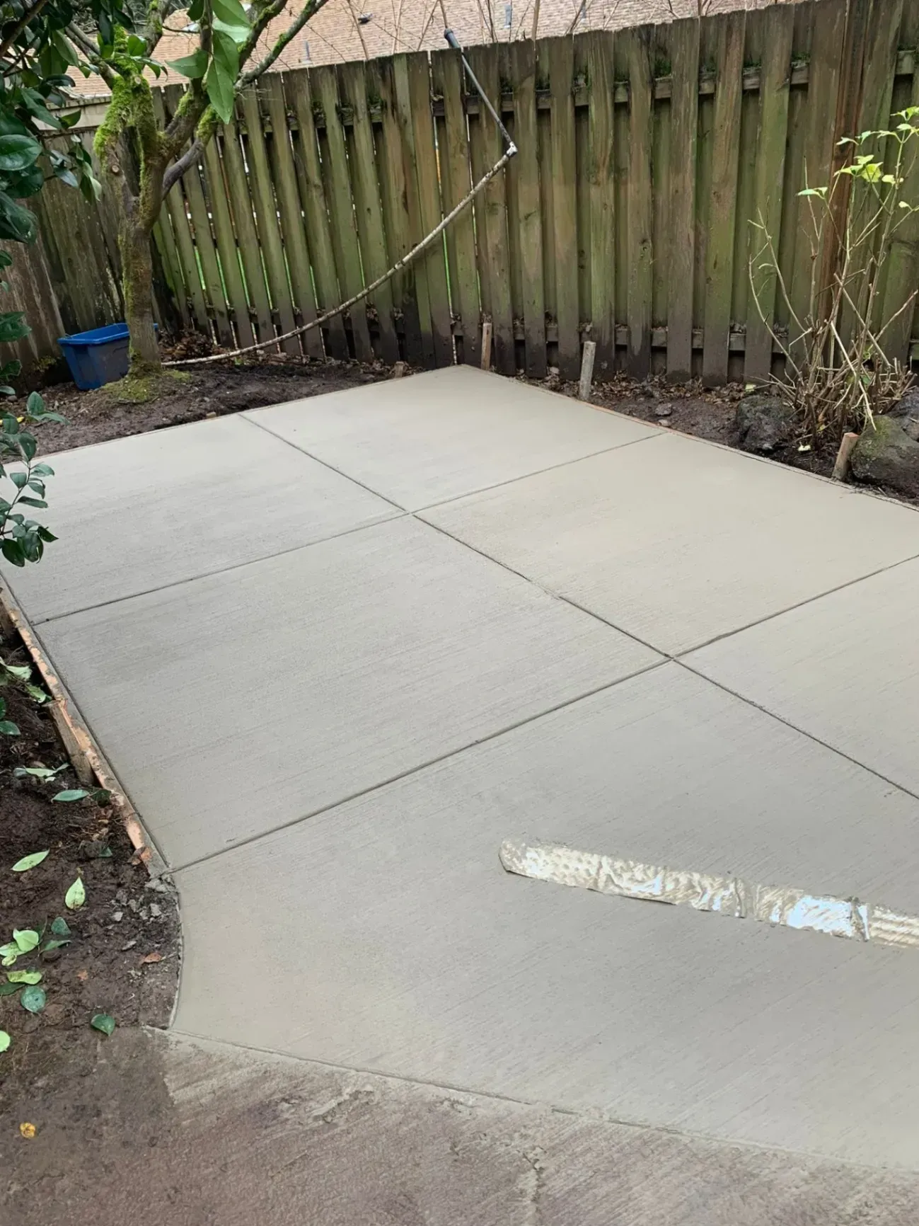 A concrete patio is being built in a backyard next to a wooden fence.