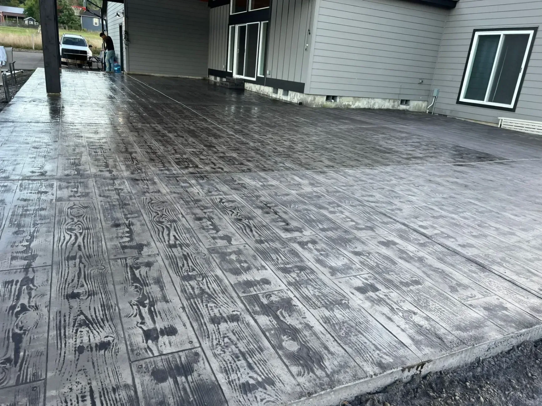A concrete driveway with a wood grain pattern is in front of a house.