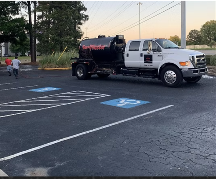 A squeegee spreading black asphalt sealer over a gray driveway surface.