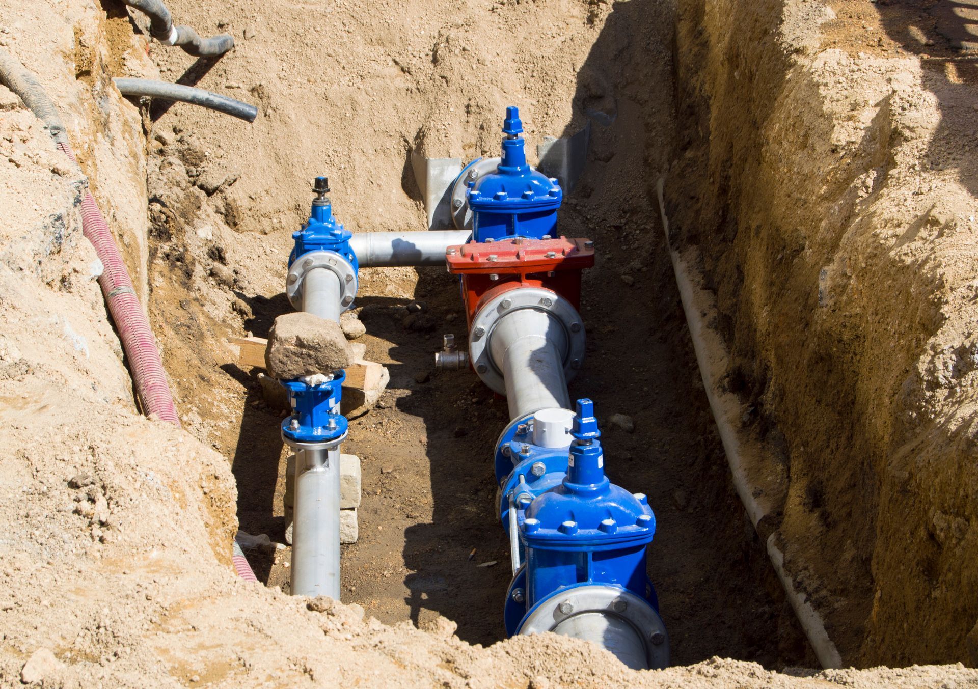 A bunch of pipes are laying in the dirt in a trench.
