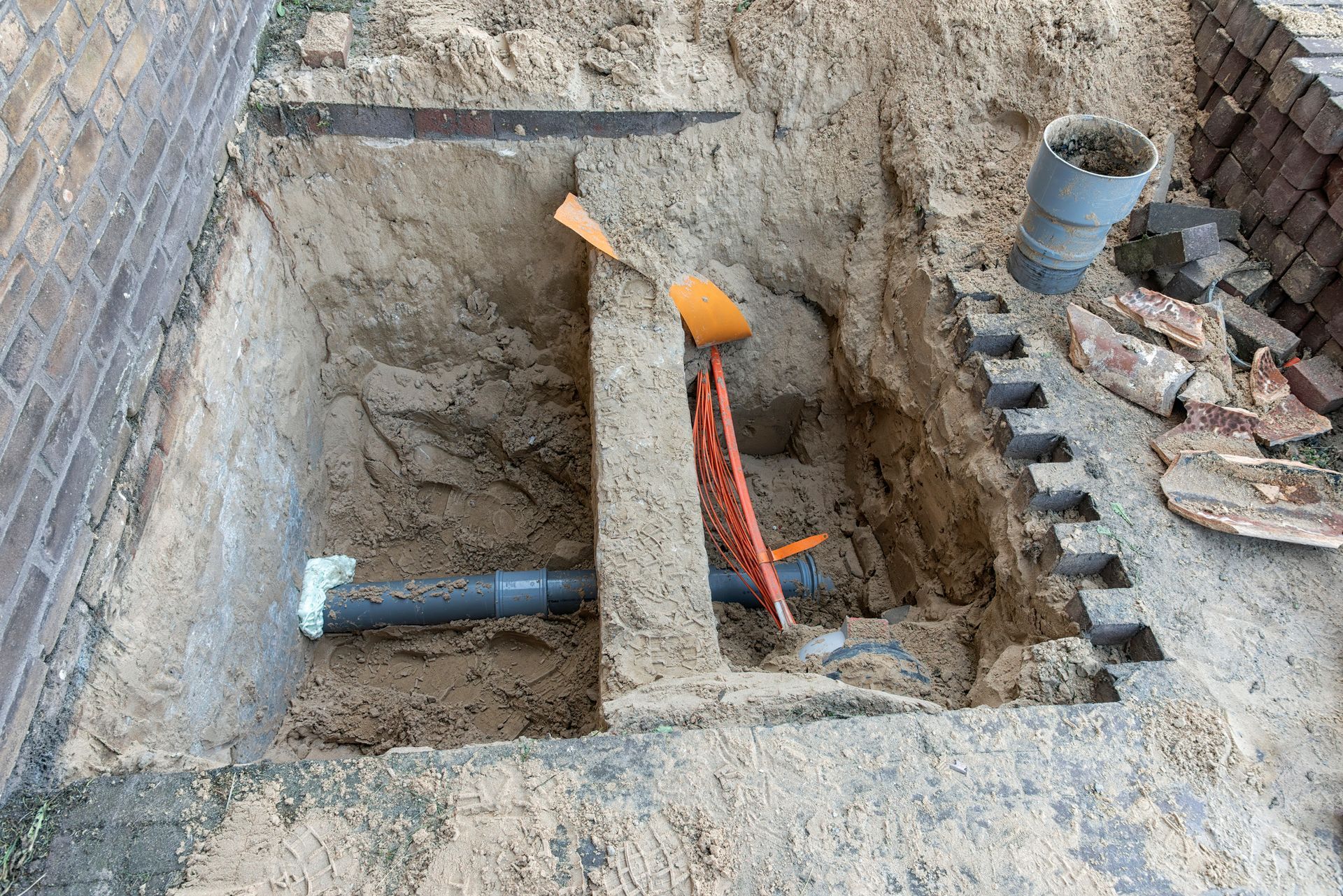 New sewer pipe in place; orange fibre cables visible near blockage area.