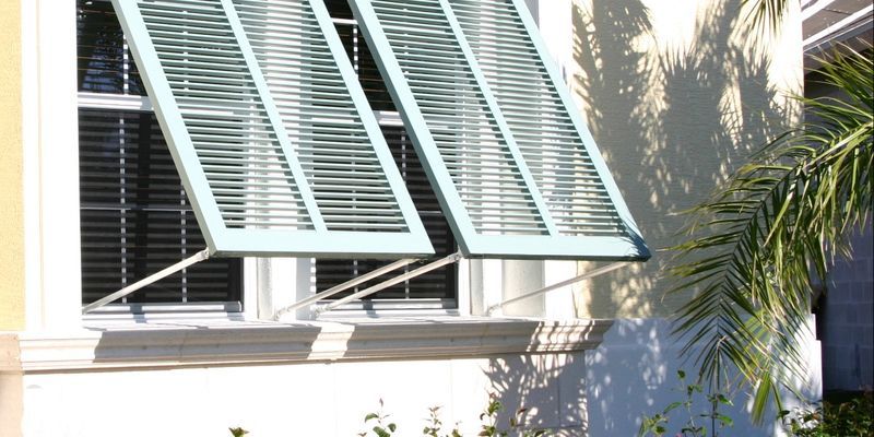 A light-blue shuttered window on a cream-colored wall; shadows of leaves cast across the wall.