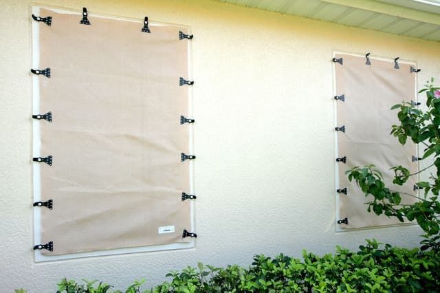 Tan hurricane shutters attached to a light-colored exterior wall.
