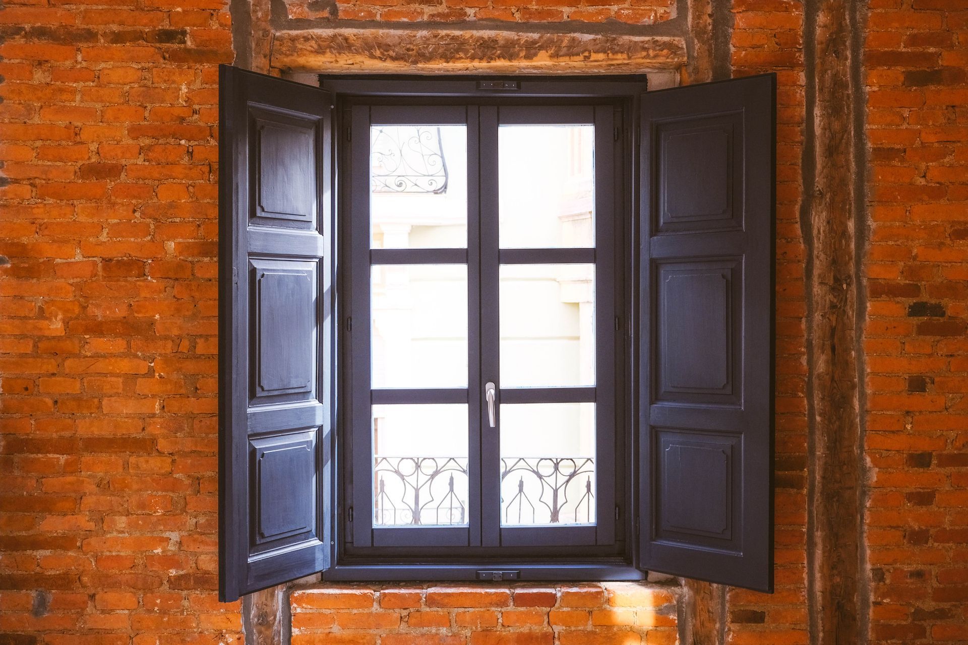 Window with open black shutters against a red brick wall.