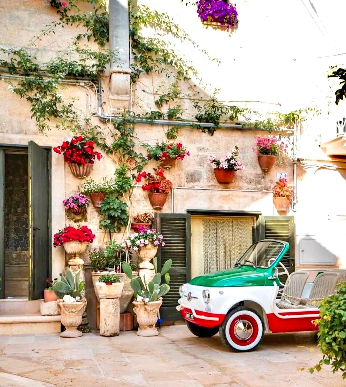 Cortile italiano con fiori colorati, auto d'epoca con i colori della bandiera italiana.