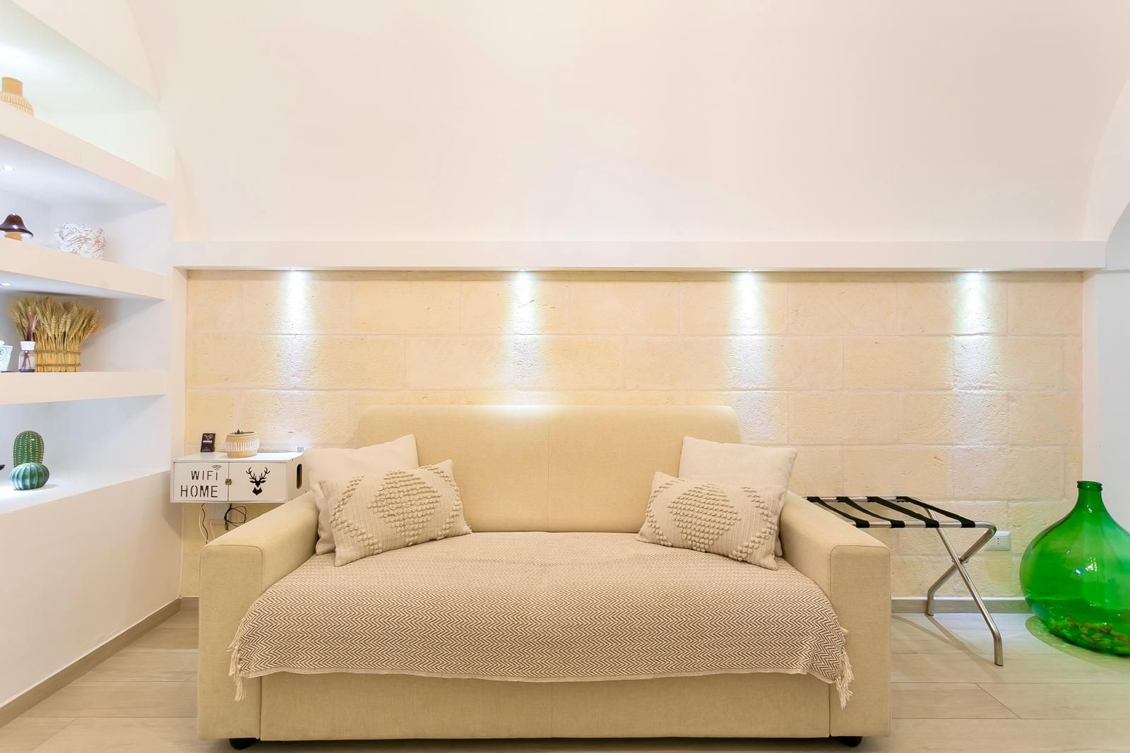 Divano beige in una stanza con parete beige testurizzata, mensole integrate e un vaso verde.