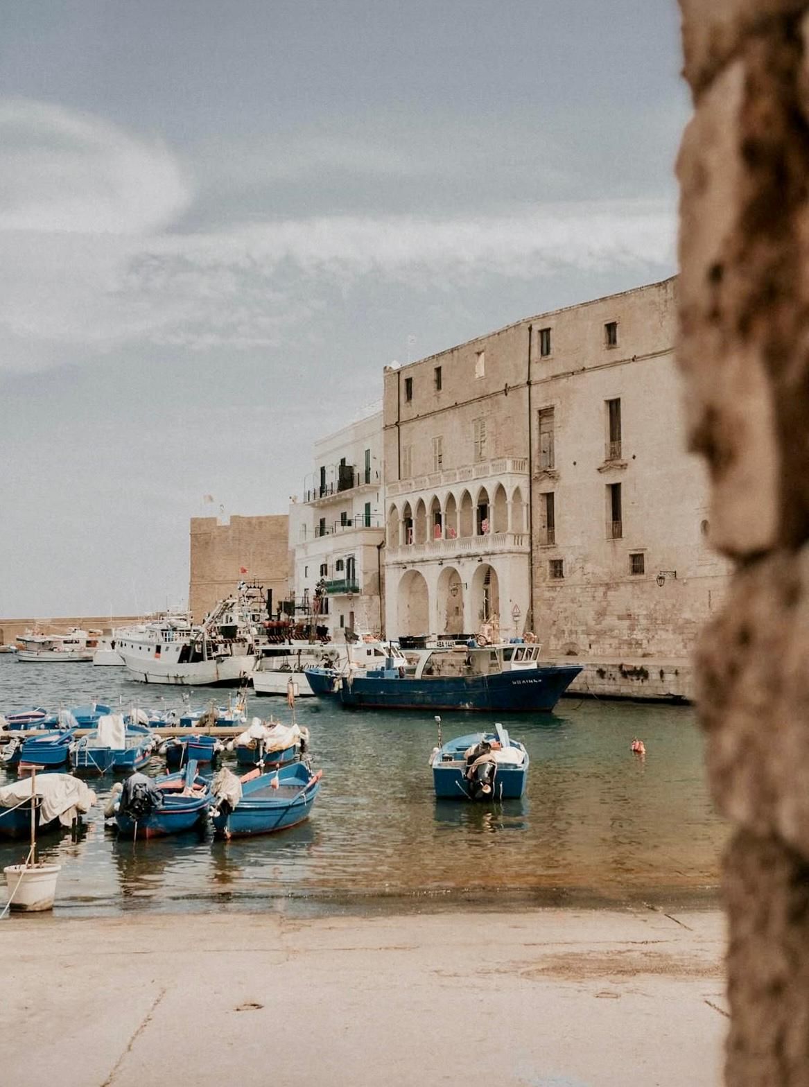 Barche nel porto con edifici beige e cielo nuvoloso.