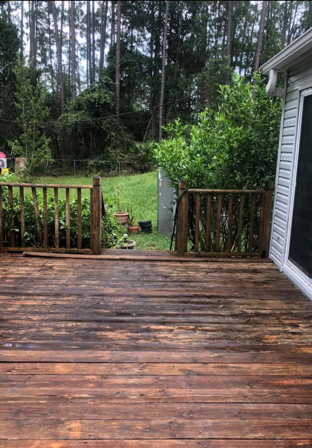 Wooden deck with weathered boards, railing, and a view of trees and yard.