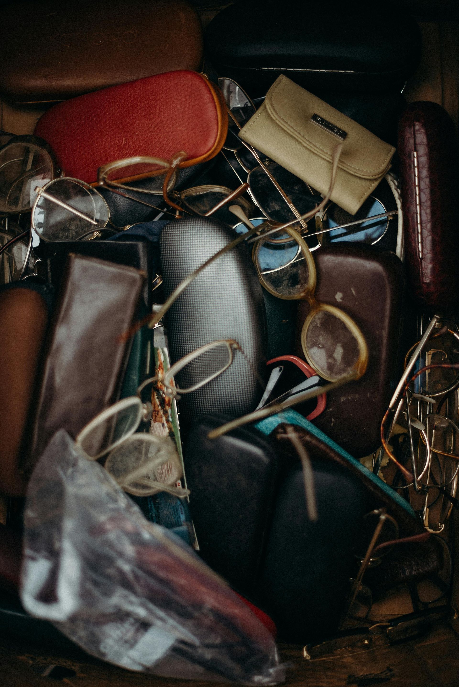 Pile of eyeglasses and cases; red, beige, and brown hues dominate.