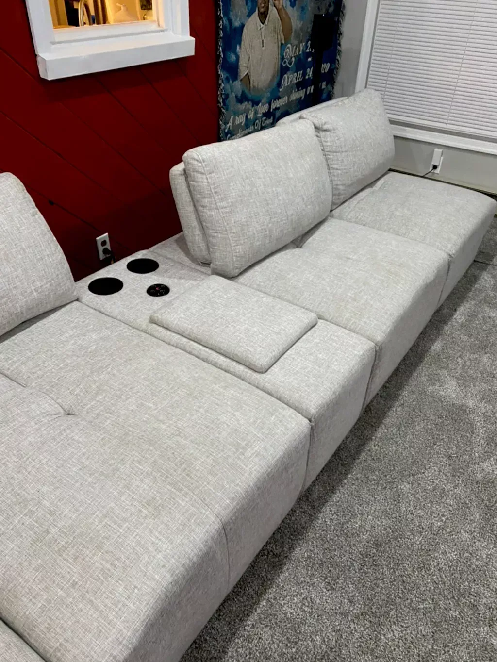 Light gray modular sofa with cup holders in a room with a red wall and carpet.