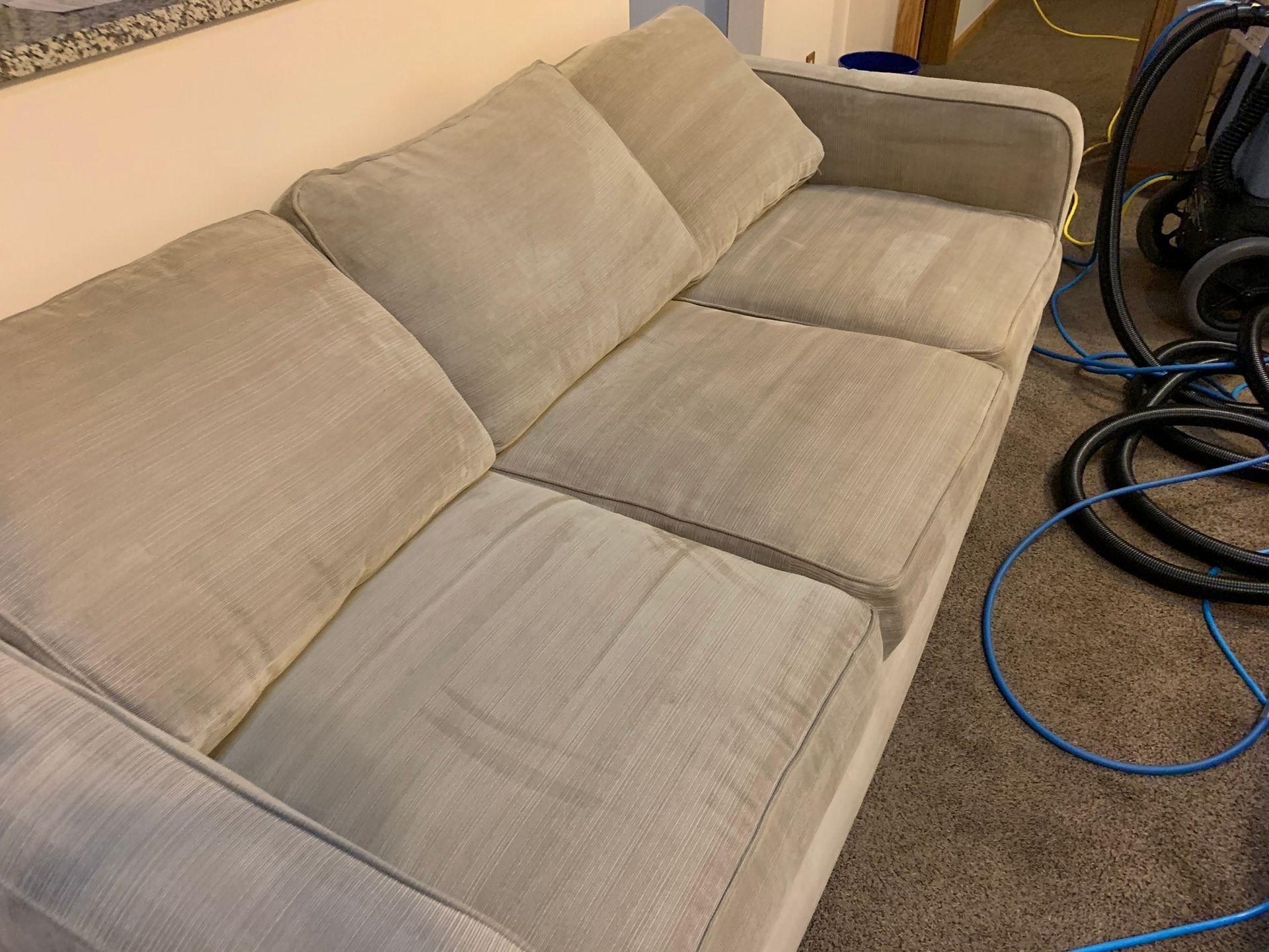 Beige couch with clean cushions, cleaning equipment in background.