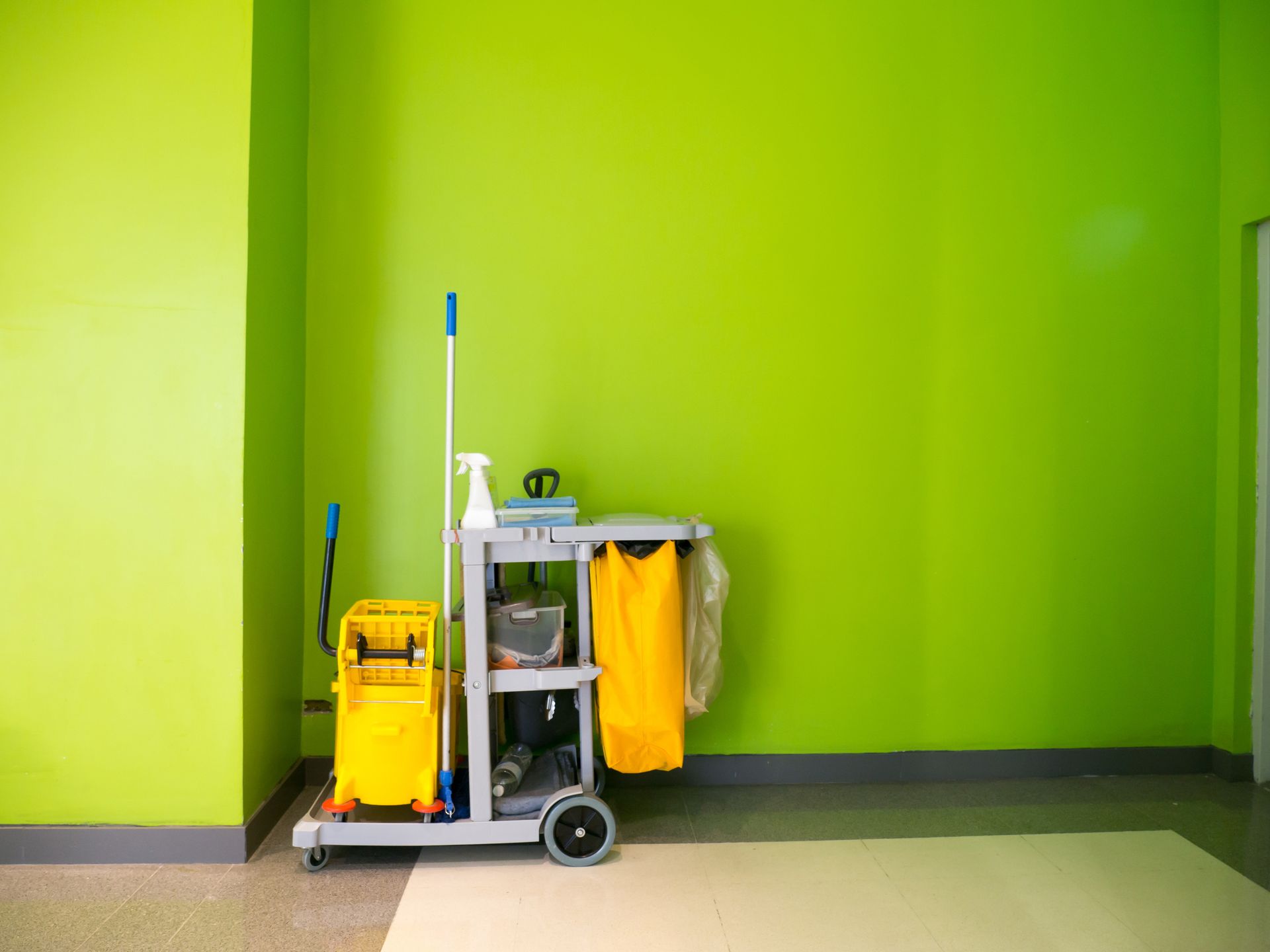 Cleaning cart against a vibrant green wall in a room with light flooring.